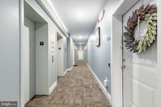 hallway featuring baseboards, elevator, and carpet