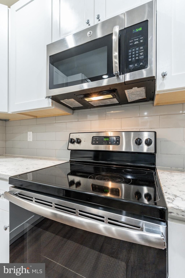 kitchen with white cabinetry, tasteful backsplash, light stone countertops, and appliances with stainless steel finishes