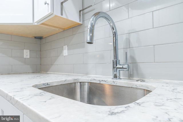 details featuring white cabinetry, tasteful backsplash, light stone countertops, and a sink