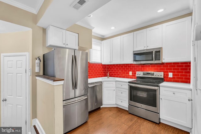 kitchen featuring white cabinetry, stainless steel appliances, backsplash, crown molding, and light hardwood / wood-style floors