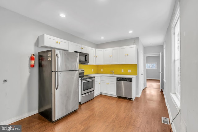 kitchen featuring backsplash, white cabinets, sink, appliances with stainless steel finishes, and light hardwood / wood-style floors