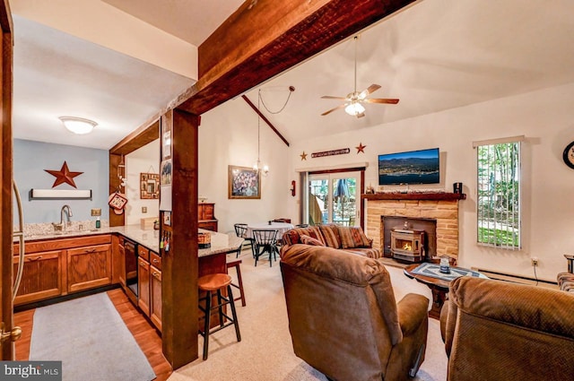 living room with a wood stove, sink, lofted ceiling with beams, light wood-type flooring, and ceiling fan