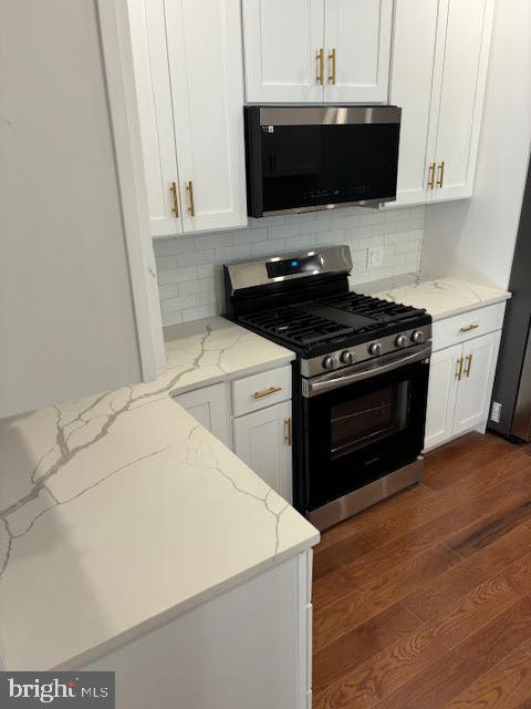 kitchen with gas stove, white cabinets, backsplash, and light stone counters