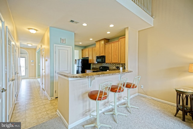 kitchen featuring tasteful backsplash, kitchen peninsula, a kitchen bar, light tile patterned floors, and black appliances