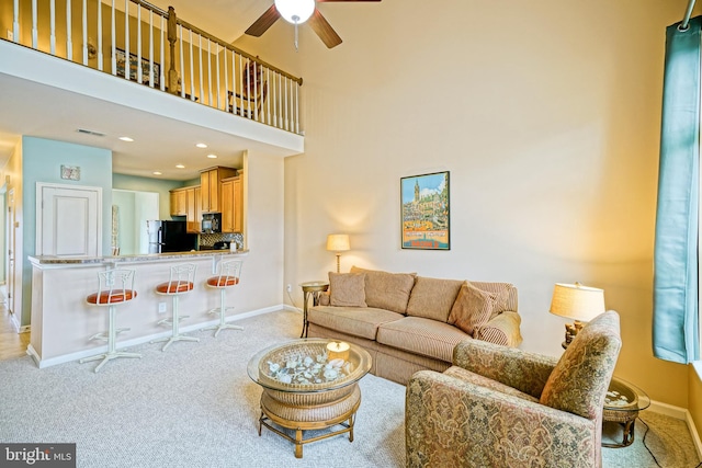 carpeted living room with ceiling fan and a high ceiling