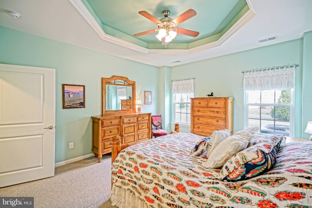 bedroom with light colored carpet, multiple windows, a tray ceiling, and ceiling fan