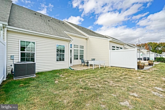 rear view of house with cooling unit, a patio area, and a lawn