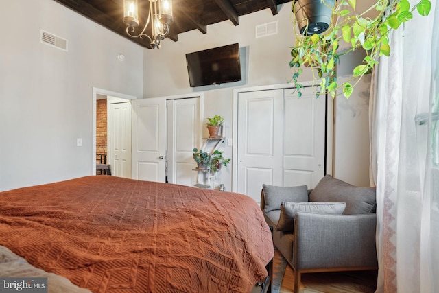 bedroom with beam ceiling, visible vents, two closets, and a chandelier