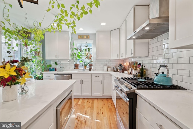 kitchen featuring white cabinets, appliances with stainless steel finishes, and wall chimney range hood