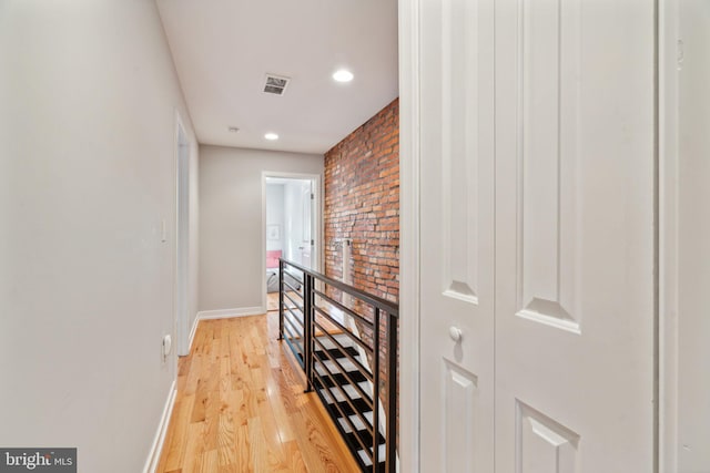 corridor with visible vents, brick wall, baseboards, an upstairs landing, and light wood-style floors