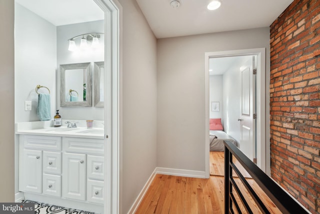 corridor featuring a sink, baseboards, brick wall, and light wood finished floors