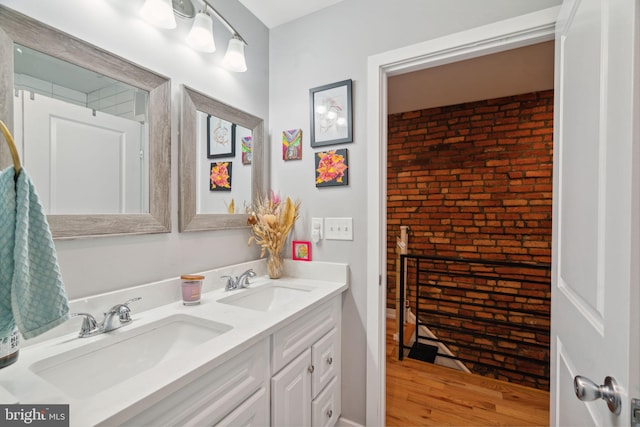 bathroom featuring double vanity, wood finished floors, brick wall, and a sink