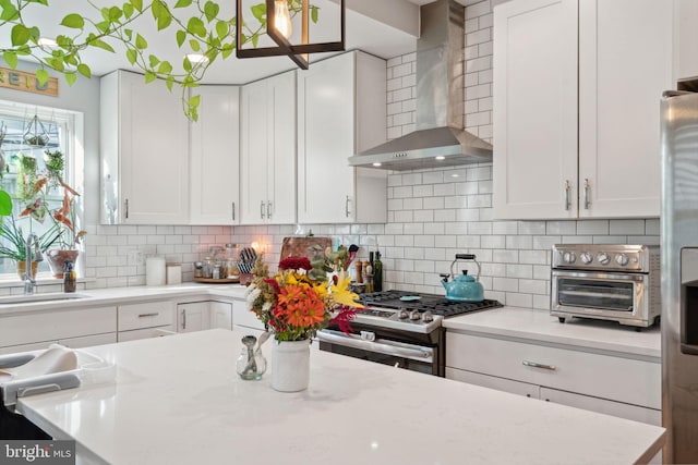 kitchen with decorative backsplash, appliances with stainless steel finishes, wall chimney exhaust hood, and white cabinetry