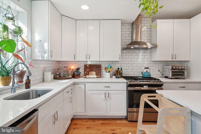 kitchen with wall chimney range hood, light countertops, light wood-style floors, stainless steel appliances, and a sink