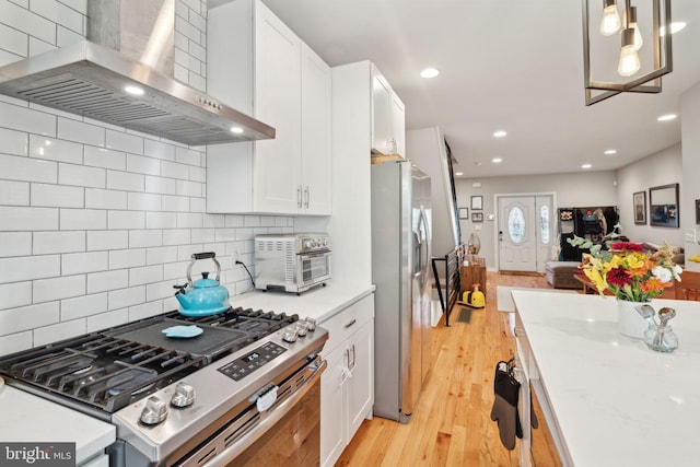 kitchen featuring light wood-type flooring, stainless steel appliances, wall chimney exhaust hood, white cabinets, and decorative backsplash