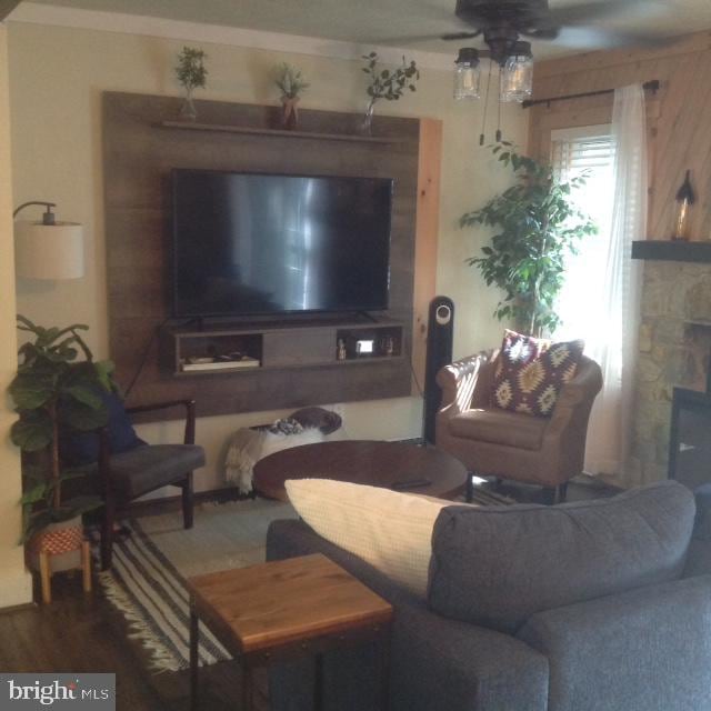 living room featuring wooden walls, a stone fireplace, hardwood / wood-style flooring, and ceiling fan