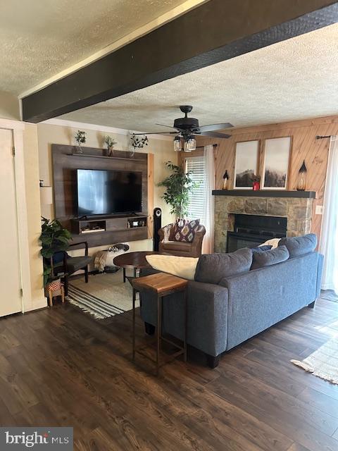 living room with dark wood-type flooring, ceiling fan, a stone fireplace, and a textured ceiling