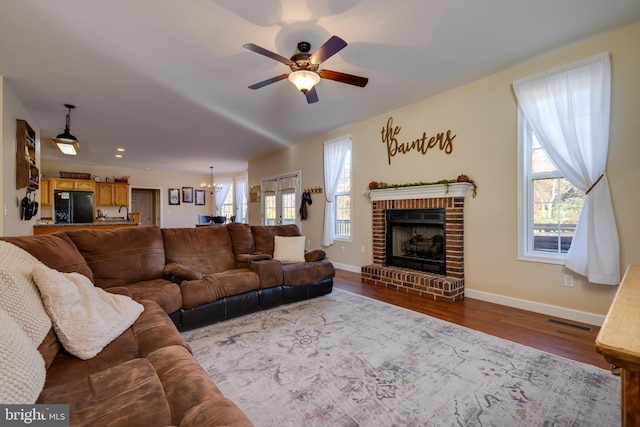 living room featuring hardwood / wood-style floors, ceiling fan with notable chandelier, plenty of natural light, and a brick fireplace