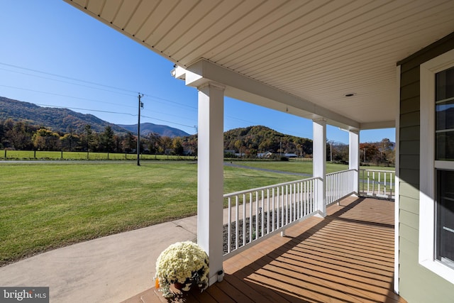 wooden deck with covered porch, a mountain view, and a lawn