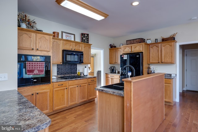 kitchen featuring black appliances, sink, backsplash, light hardwood / wood-style flooring, and a kitchen island with sink