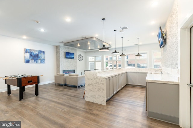 kitchen featuring kitchen peninsula, a large fireplace, sink, decorative light fixtures, and light wood-type flooring