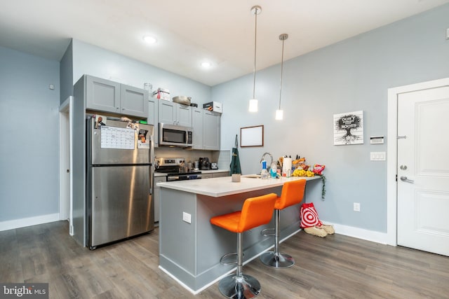 kitchen featuring a kitchen bar, dark hardwood / wood-style floors, stainless steel appliances, gray cabinetry, and decorative light fixtures