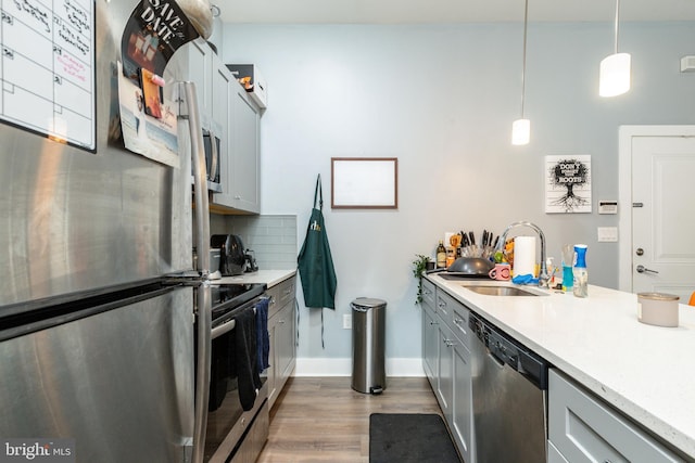 kitchen with tasteful backsplash, appliances with stainless steel finishes, sink, hardwood / wood-style floors, and decorative light fixtures