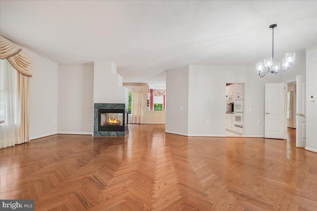 unfurnished living room featuring light parquet flooring, a chandelier, and a multi sided fireplace