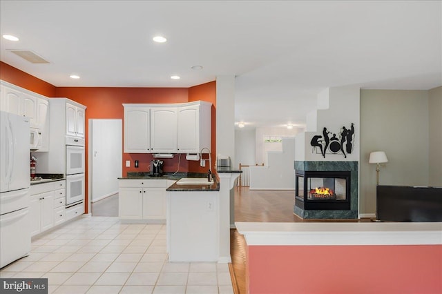 kitchen with a multi sided fireplace, a kitchen island, white cabinets, and white appliances