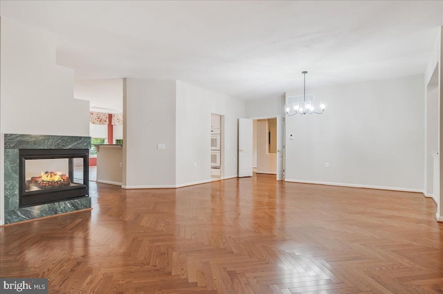 unfurnished living room featuring a premium fireplace, an inviting chandelier, and light parquet flooring