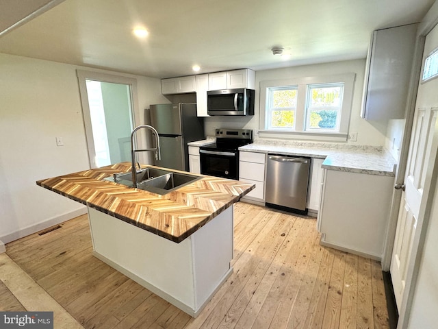 kitchen featuring white cabinetry, sink, appliances with stainless steel finishes, light hardwood / wood-style flooring, and a kitchen island