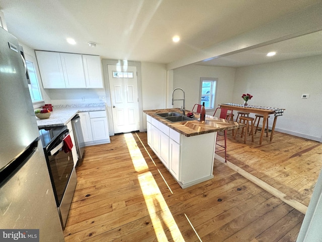 kitchen with stainless steel appliances, light hardwood / wood-style floors, sink, and a kitchen island with sink