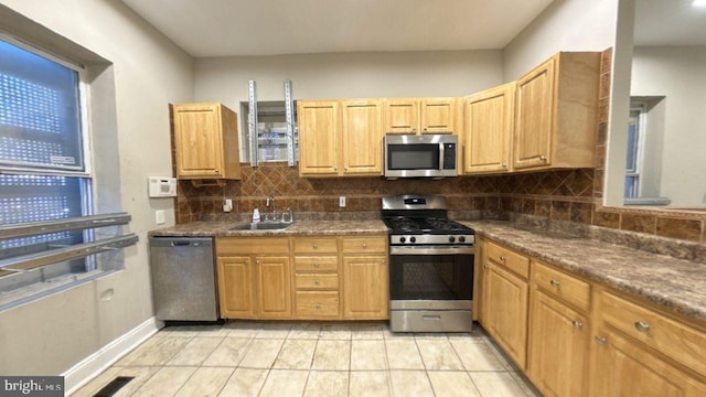 kitchen with decorative backsplash, light tile patterned floors, appliances with stainless steel finishes, dark stone countertops, and sink