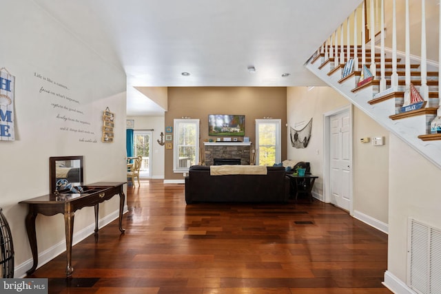 living room with dark hardwood / wood-style floors, a healthy amount of sunlight, and a stone fireplace