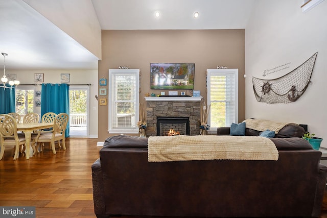 living room featuring hardwood / wood-style flooring, a stone fireplace, and a chandelier