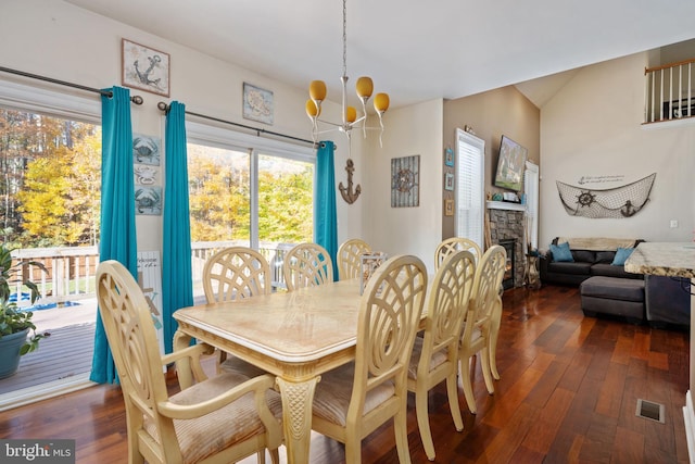 dining space with a stone fireplace, dark hardwood / wood-style flooring, and a notable chandelier