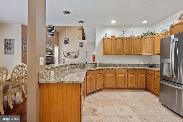 kitchen with sink, stainless steel fridge, hanging light fixtures, light stone counters, and kitchen peninsula