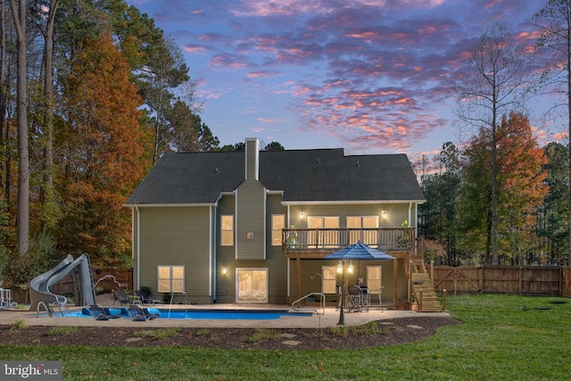 back house at dusk featuring a yard, a patio, and a swimming pool side deck