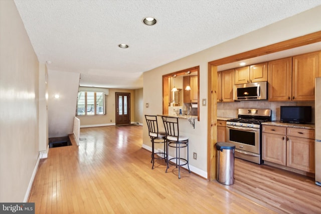 kitchen featuring appliances with stainless steel finishes, light hardwood / wood-style flooring, a textured ceiling, and a kitchen bar