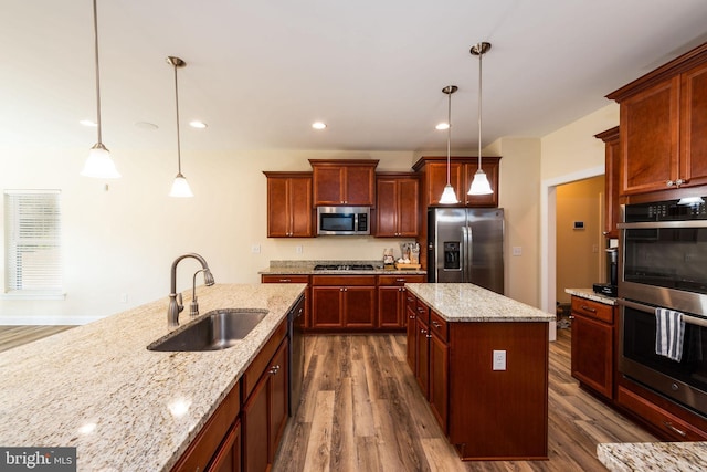 kitchen with dark wood-type flooring, stainless steel appliances, sink, a center island, and decorative light fixtures