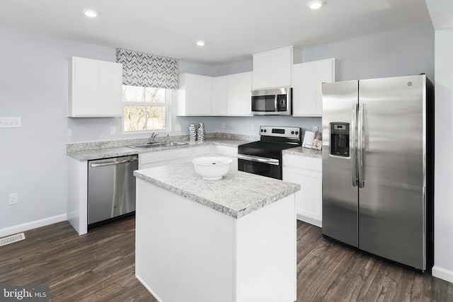 kitchen with appliances with stainless steel finishes, a kitchen island, dark wood-type flooring, sink, and white cabinetry