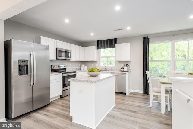 kitchen with white cabinets, a center island, stainless steel appliances, and light hardwood / wood-style floors