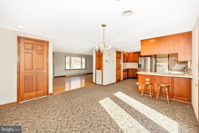 kitchen featuring washing machine and dryer, a baseboard heating unit, kitchen peninsula, a kitchen breakfast bar, and stainless steel fridge with ice dispenser