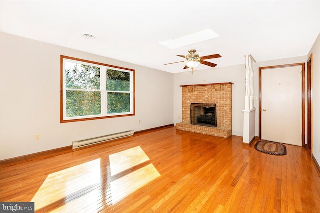 unfurnished living room with baseboard heating, hardwood / wood-style floors, a brick fireplace, and a skylight