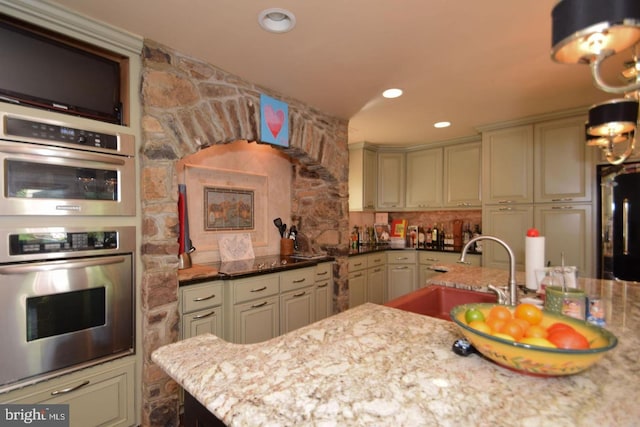 kitchen with stainless steel double oven, a sink, recessed lighting, and light stone countertops