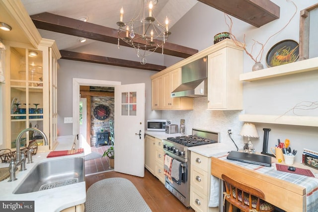 kitchen featuring stainless steel gas range oven, lofted ceiling with beams, wall chimney exhaust hood, light countertops, and a sink