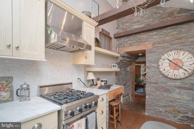 kitchen featuring stainless steel range with gas cooktop, open shelves, light countertops, decorative backsplash, and wall chimney range hood