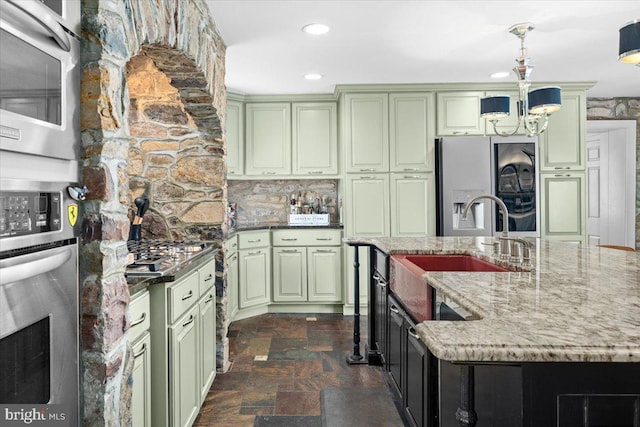 kitchen with a sink, green cabinets, appliances with stainless steel finishes, stone finish flooring, and decorative light fixtures