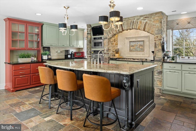 kitchen featuring glass insert cabinets, a kitchen island with sink, stone tile flooring, pendant lighting, and a sink