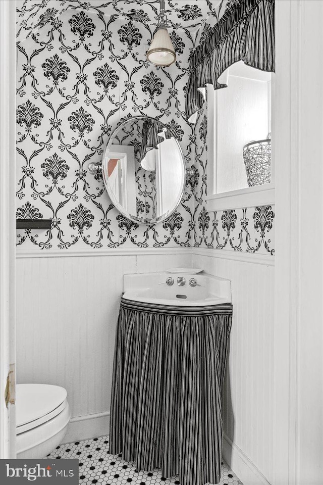 bathroom featuring tile patterned flooring, a wainscoted wall, toilet, and wallpapered walls